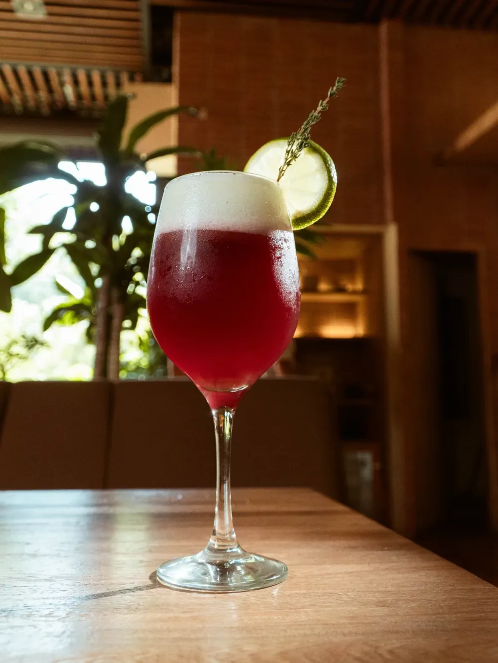 Copa de bebida roja con espuma y cítrico sobre la barra