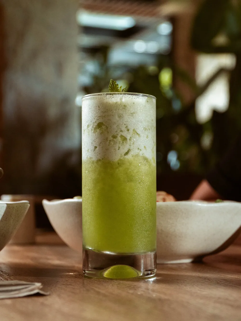 Vaso alto de bebida verde con limón sobre la mesa